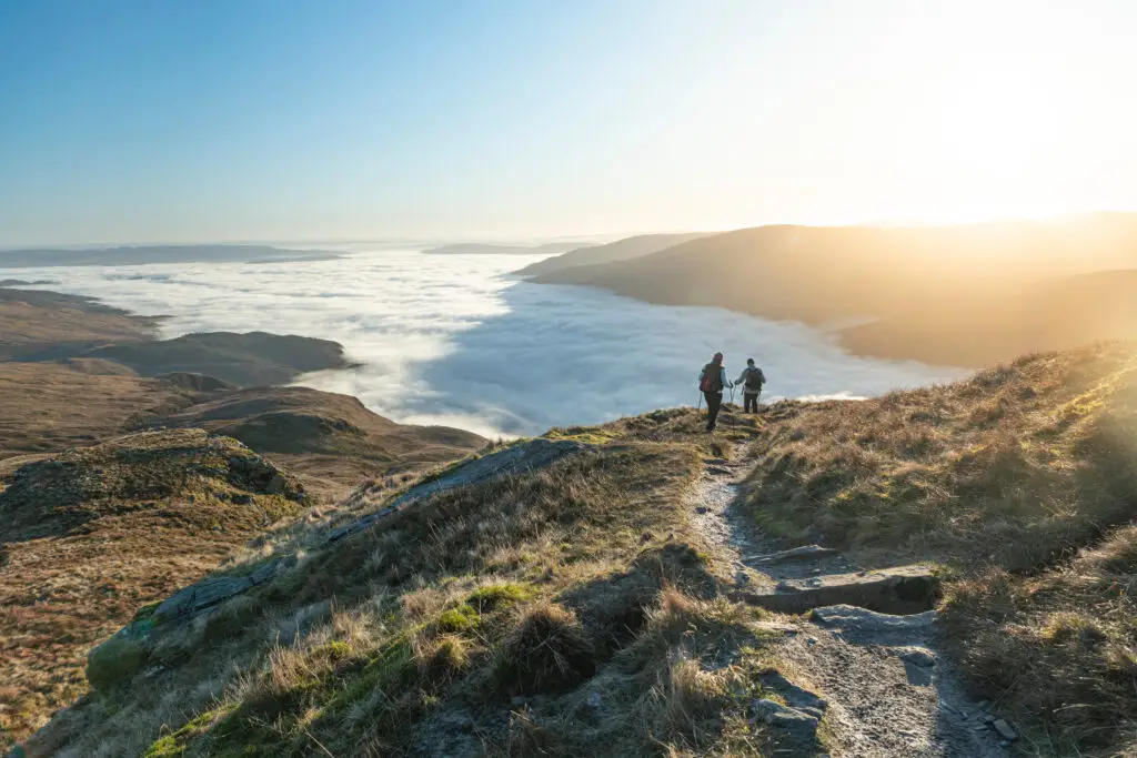 Hikers walking along a scenic mountain trail on Ben Lomond overlooking Loch Lomond and the Trossachs National Park at sunrise in the Scottish Highlands, Scotland