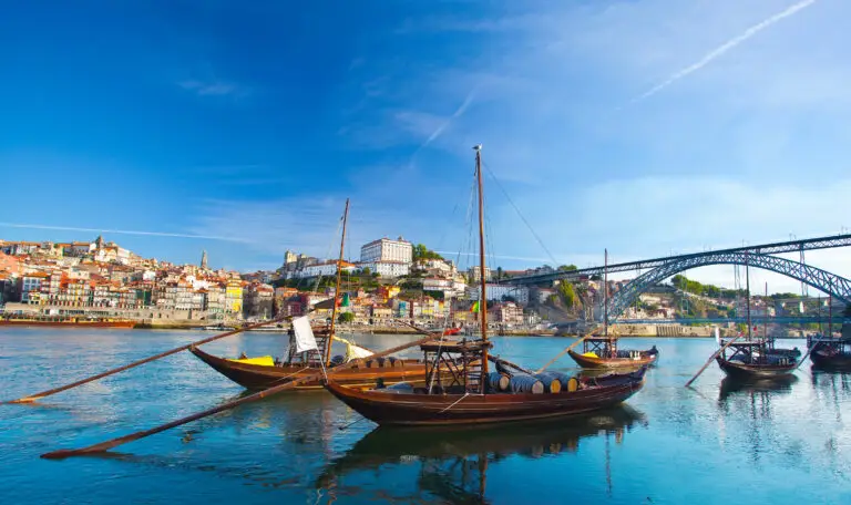 Traditional rabelo boats on the Douro River with the Dom Luís I Bridge and colorful Ribeira district in Oporto, Portugal