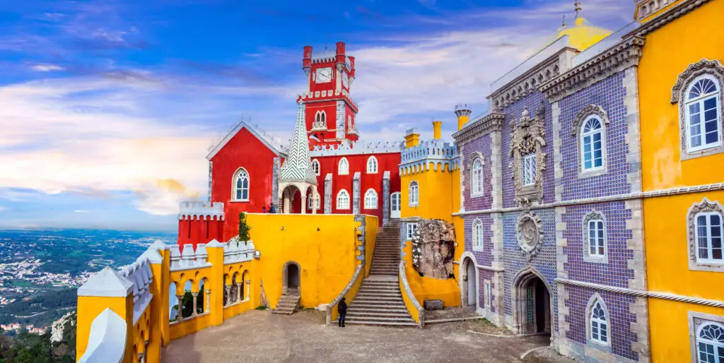 Colorful courtyard and vibrant architecture of Pena Palace in Sintra, Portugal, showcasing red and yellow towers under a blue sky, UNESCO World Heritage Site and top tourist attraction near Lisbon