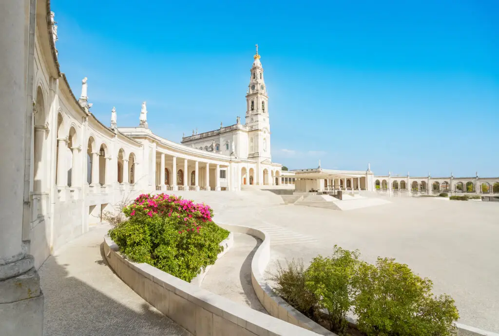 Sanctuary of Our Lady of Fátima in Portugal with basilica, colonnade, and courtyard under a bright blue sky, a popular pilgrimage and sightseeing destination in Europe
