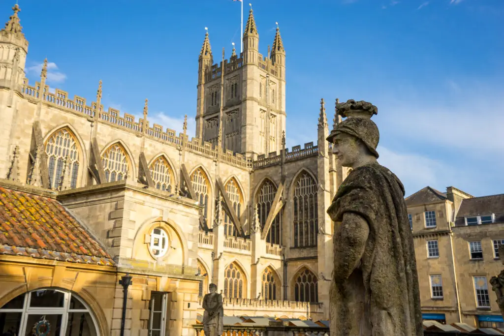 Historic Bath Abbey and Roman statue under blue sky in Bath, England, a popular tourist attraction and UNESCO World Heritage site