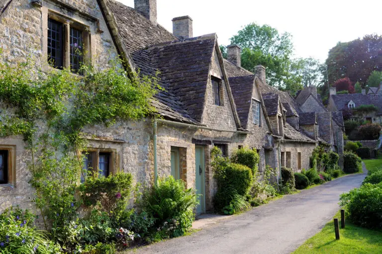 Historic stone cottages along a scenic village lane in the Cotswolds, England, showcasing traditional English countryside architecture and charm