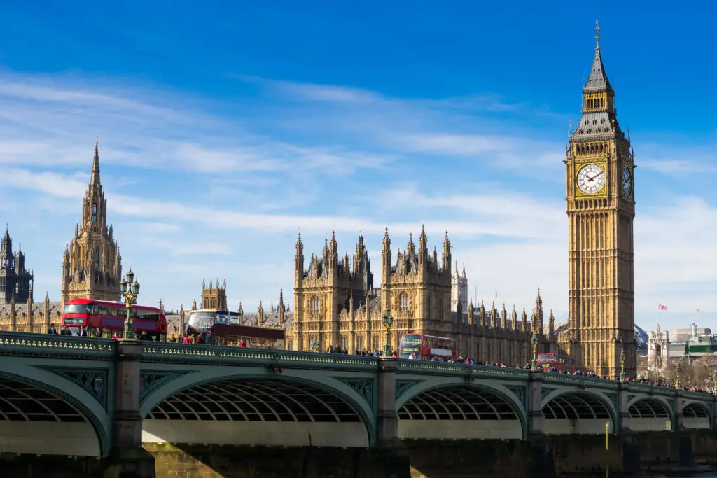 Big Ben and the Houses of Parliament in London England with red double-decker buses crossing Westminster Bridge on a sunny day