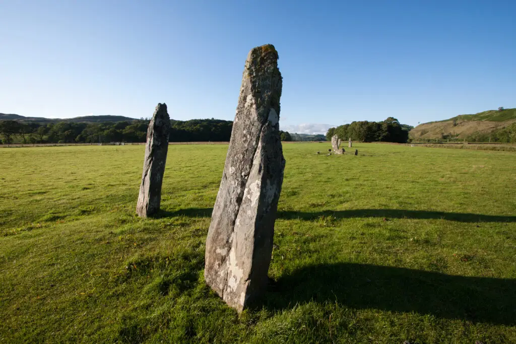 Ancient Nether Largie Standing Stones in Kilmartin Glen, Scotland, surrounded by green fields and hills under a clear blue sky, a popular historical site for tours in Europe