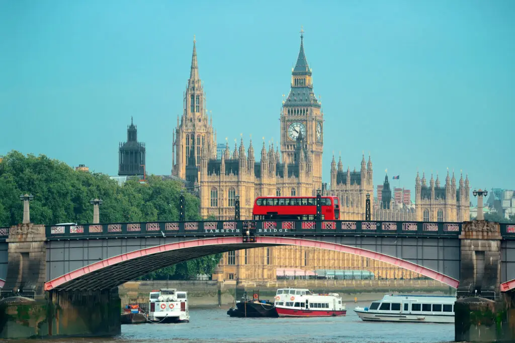 Red double-decker bus crossing Lambeth Bridge with the Palace of Westminster and Big Ben in the background, London England