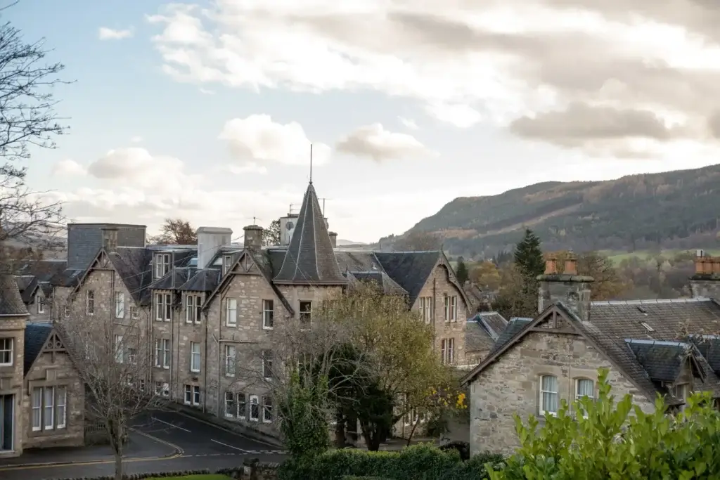 Historic stone buildings in Pitlochry, Scotland with scenic hillside landscape in the background, showcasing traditional Scottish architecture and countryside charm