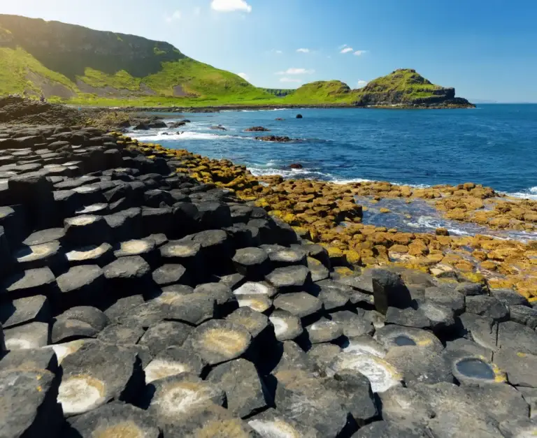 Giant’s Causeway basalt columns along the Atlantic coast in Northern Ireland with scenic cliffs and blue ocean under a sunny sky