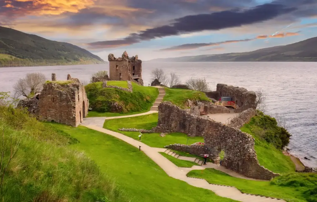 Urquhart Castle ruins overlooking Loch Ness in the Scottish Highlands at sunset, popular historic attraction featured on Braw Scottish Tours