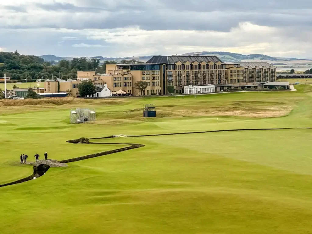 View of the Old Course golf course and the Swilcan Bridge at St Andrews, Scotland, with the Old Course Hotel in the background under a cloudy sky