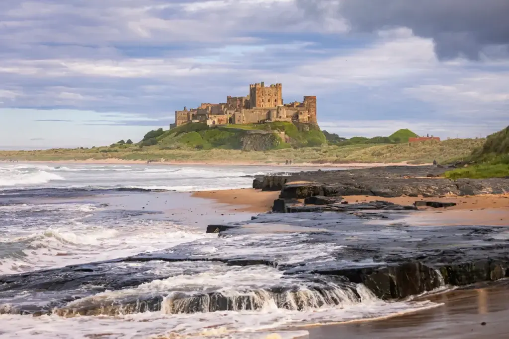 Bamburgh Castle overlooking the beach and North Sea coastline in Bamburgh, England, a popular historic attraction near the Scottish border featured in Braw Scottish Tours