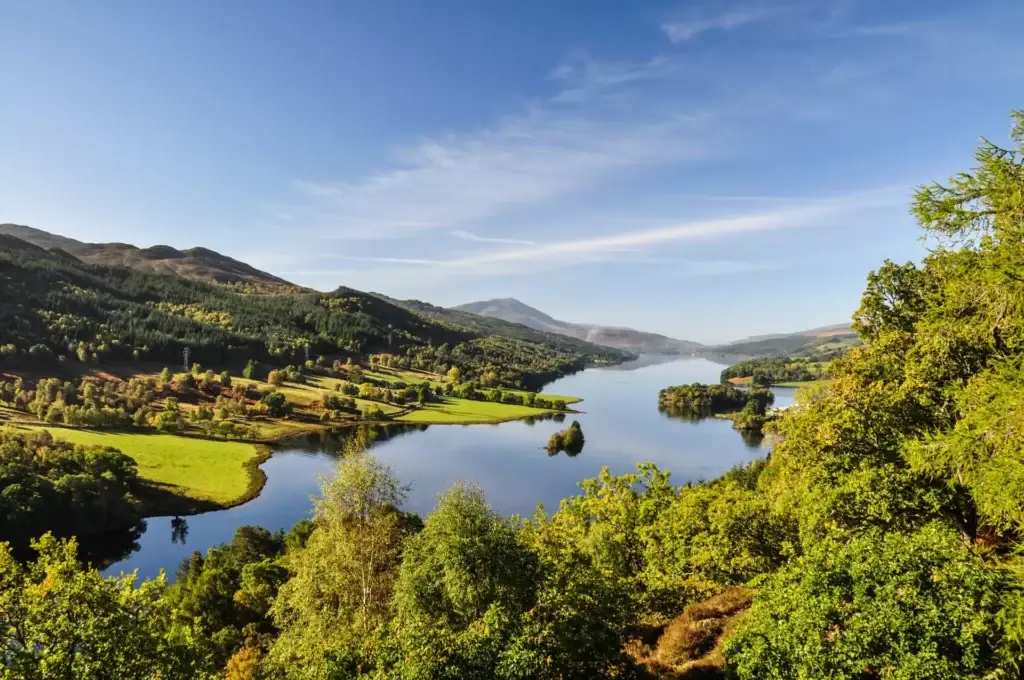 Scenic view of Queen’s View in Scotland overlooking Loch Tummel with lush green hills, forests, and distant mountains under a bright blue sky