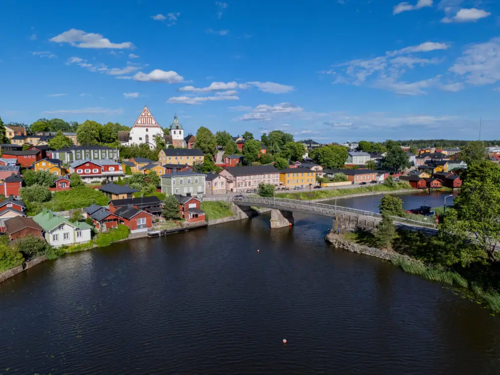 Scenic view of Old Town Porvoo in Finland with colorful wooden houses, historic church, and stone bridge over the Porvoo River on a sunny summer day