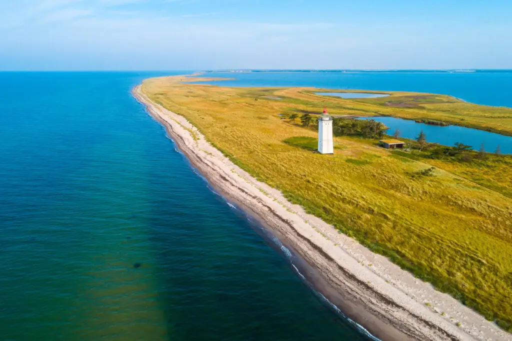 Aerial view of Hyllekrog Fyr lighthouse on the scenic coastline of Lolland, Denmark with blue sea and grassy dunes, popular tourist attraction in Denmark