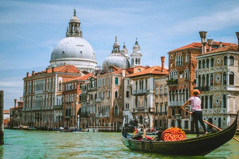 Gondolier rowing a gondola on the Grand Canal with historic buildings and Santa Maria della Salute in Venice, Italy