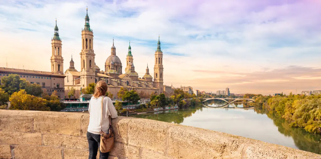 Tourist admiring Basilica of Our Lady of the Pillar from Puente de Piedra bridge over the Ebro River in Zaragoza, Spain at sunset