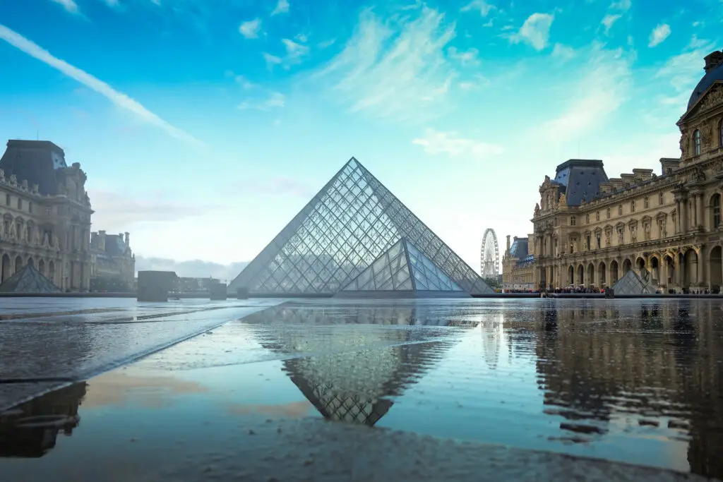 Louvre Museum glass pyramid in Paris France reflecting on wet courtyard with blue sky backdrop perfect for Europe private tours and Paris sightseeing