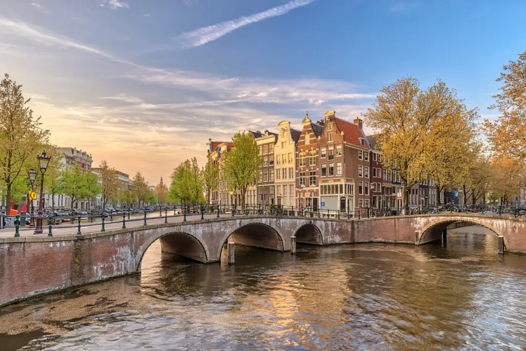 Amsterdam canal and historic houses at sunset with bridge and reflections on the water, Netherlands city skyline travel destination