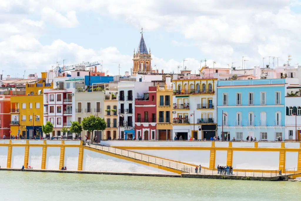 Colorful riverside buildings in the Triana neighborhood of Seville, Spain, viewed across the Guadalquivir River on a sunny day