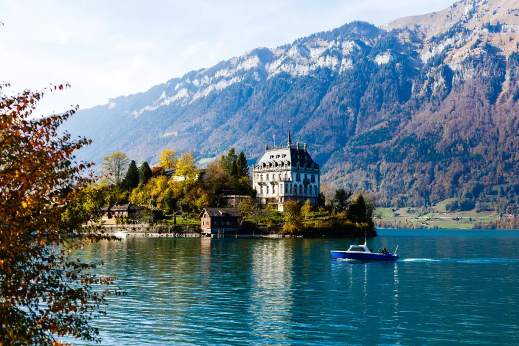 Autumn view of Interlaken in Switzerland with a historic lakeside mansion, boat on Lake Brienz, and the Swiss Alps mountains in the background