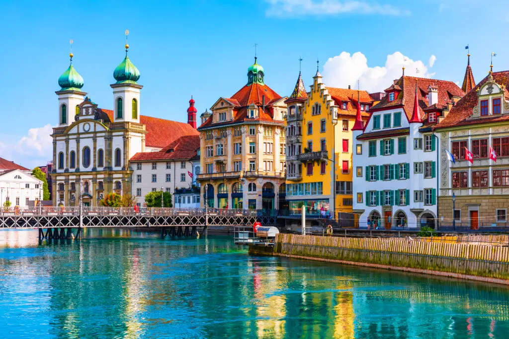 Colorful historic buildings along the Reuss River in Lucerne Switzerland with Jesuit Church and Chapel Bridge reflected in the water