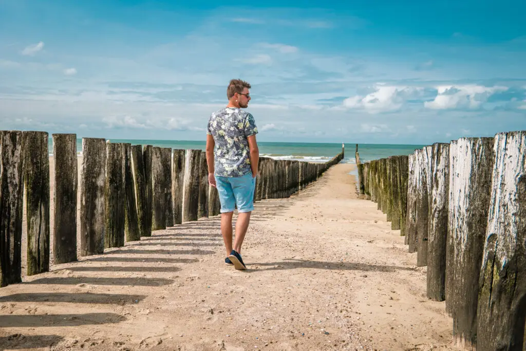 Man walking along sandy beach with wooden poles by the sea in Domburg, Zeeland, The Netherlands, on a sunny day