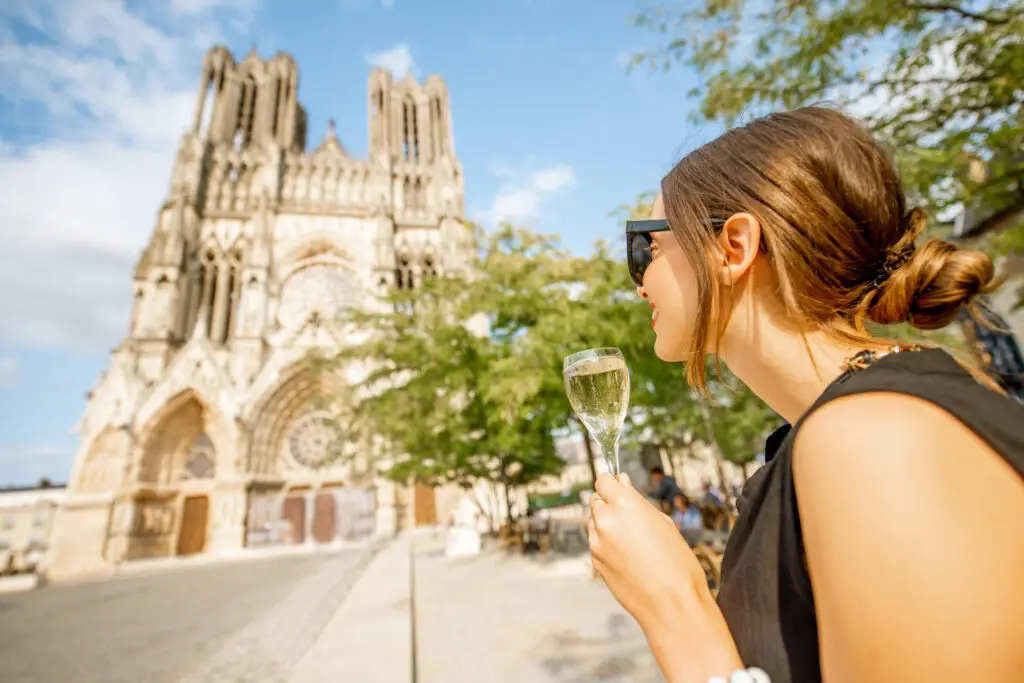 Young woman enjoying a glass of champagne in front of the Reims Cathedral in France during a Europe private tour experience