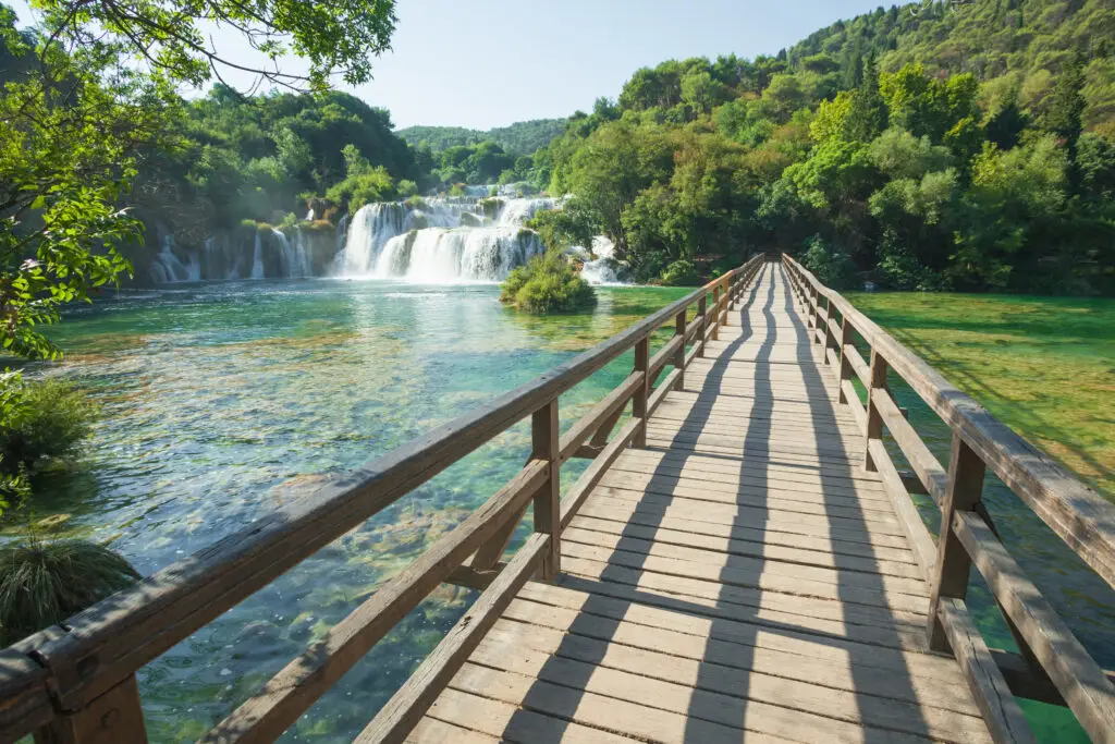 Wooden bridge over turquoise water leading to waterfalls at Krka National Park, Croatia surrounded by lush green forest