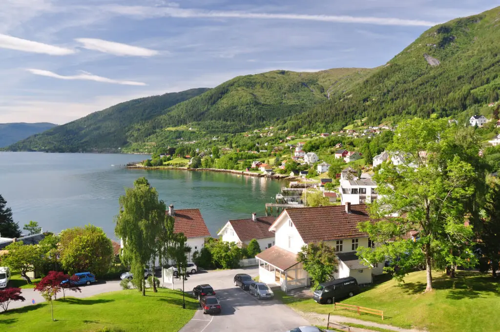 Scenic view of Balestrand Norway with colorful houses, lush green hills, and fjord waters on a sunny day, popular tourist destination for Norwegian fjord tours