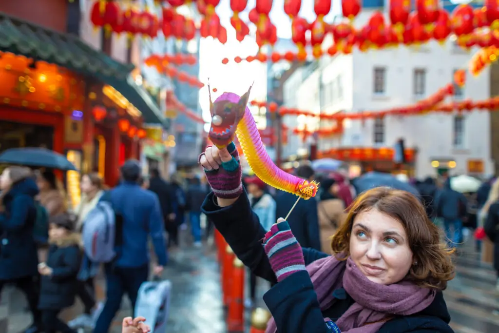 Woman holding a colorful paper dragon at Chinese New Year celebrations in London Chinatown, England, during a festive European city tour