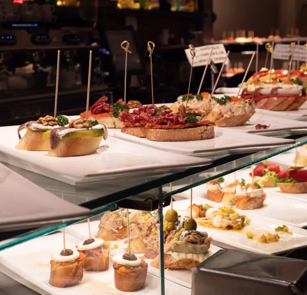 Assortment of traditional Spanish tapas sandwiches displayed in a glass showcase at a bar in Spain