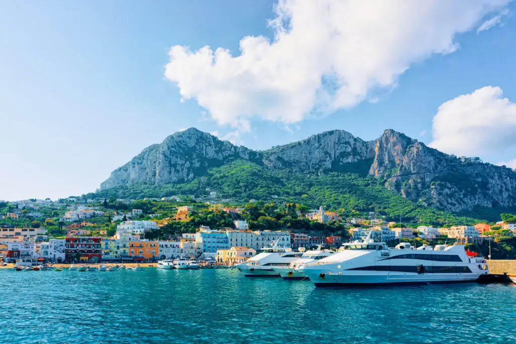 Marina with luxury yachts in Capri Island town near Naples, Italy, with colorful seaside buildings and scenic mountains in the background, popular Mediterranean travel destination