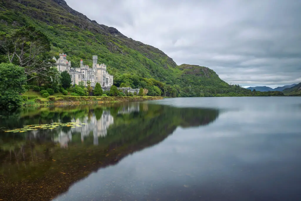 Kylemore Abbey in Connemara County Galway Ireland reflected in calm lake surrounded by lush green hills and scenic landscape