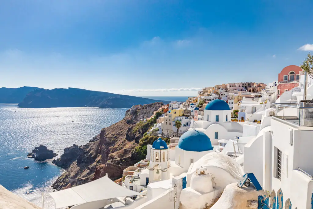 Scenic view of Oia village in Santorini, Greece with whitewashed buildings, blue-domed churches, and the Aegean Sea under a bright blue sky