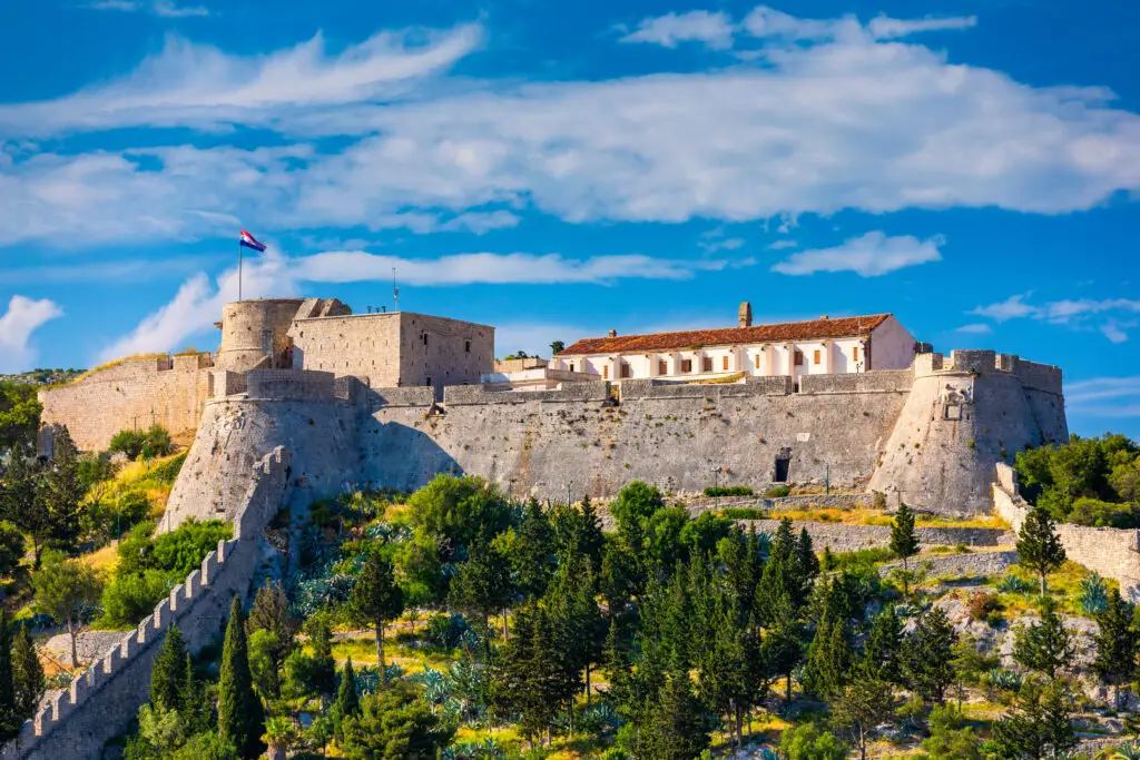 Fortica Fortress, also known as Spanish Fort or Spanjola Fortress, overlooking Hvar Town on the island of Hvar, Croatia, with stone walls, lush greenery, and a clear blue sky.