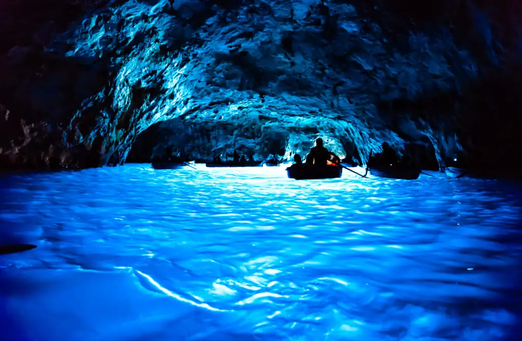 Boats exploring the glowing blue waters inside the Grotta Azzurra sea cave on Capri Island, Italy, a famous European tourist attraction