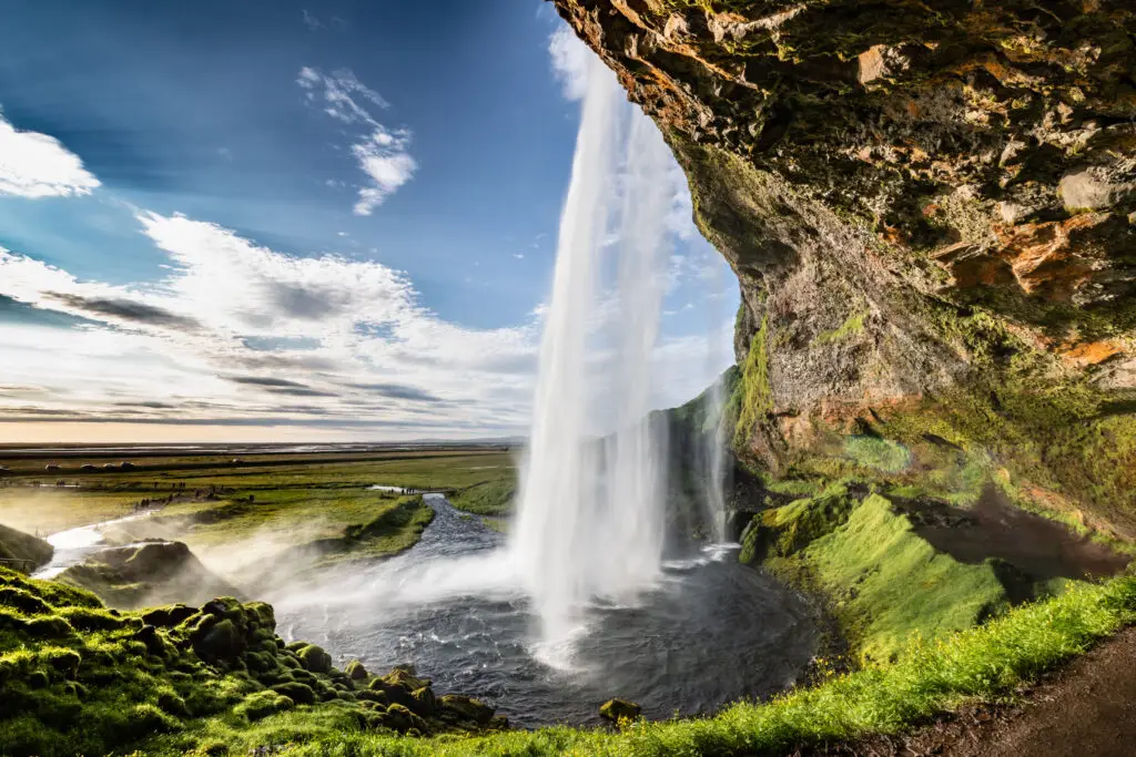 Seljalandsfoss waterfall in Iceland with lush green cliffs, flowing river, and dramatic sky, a popular tourist attraction on Iceland private tours
