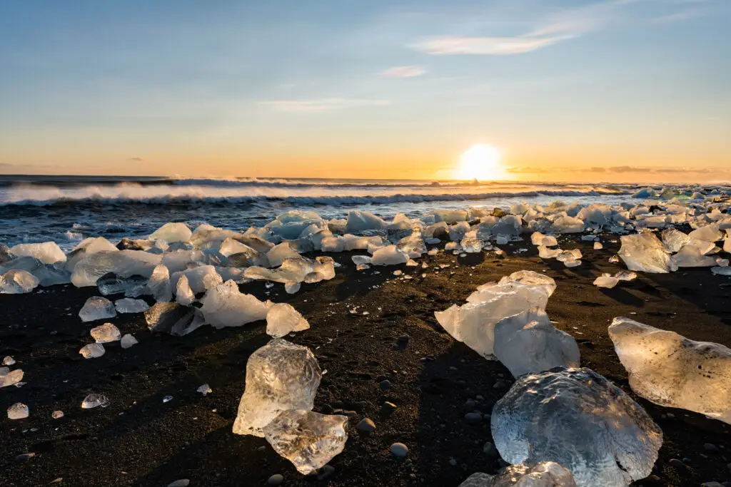 Glacial ice chunks sparkling on the black sand of Diamond Beach in Iceland at sunrise, a popular tourist attraction near Jökulsárlón Glacier Lagoon