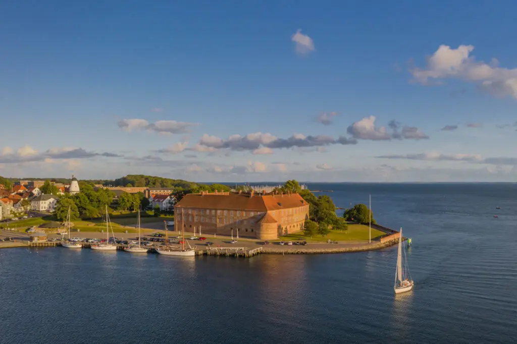 Sailboat entering the harbor near a historic brick fortress and coastal town in Denmark, scenic European seaside view for private tours