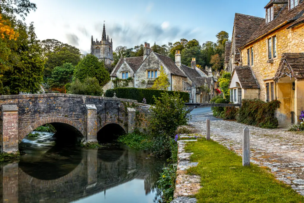 Picturesque view of Castle Combe village in the Cotswolds, England, featuring a historic stone bridge, traditional cottages, and scenic countryside architecture
