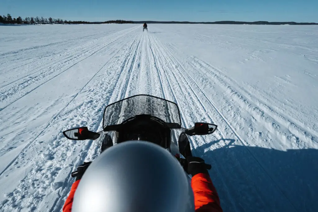 Woman riding a snowmobile across a snowy landscape in Europe during a winter motor sled race tour
