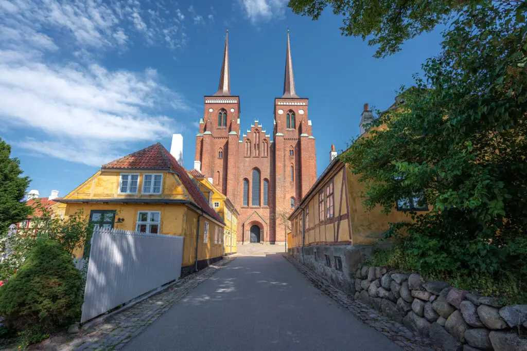Roskilde Cathedral in Denmark with its twin spires and historic architecture surrounded by colorful traditional houses on a sunny day