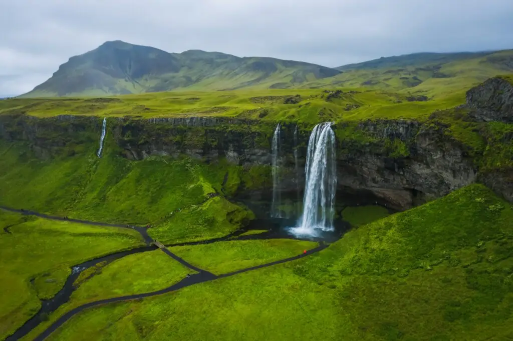 Seljalandsfoss waterfall in Iceland surrounded by lush green cliffs and scenic walking paths, a popular tourist attraction on the South Coast of Iceland