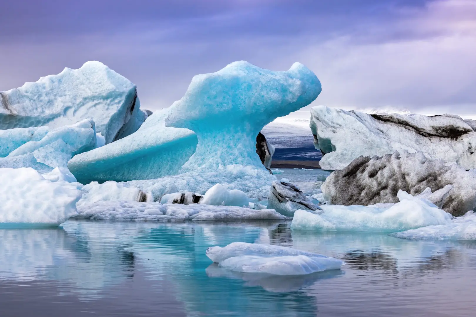 Massive blue icebergs floating in the Jokulsarlon Glacial Lagoon in Iceland with reflections on calm water under a cloudy sky