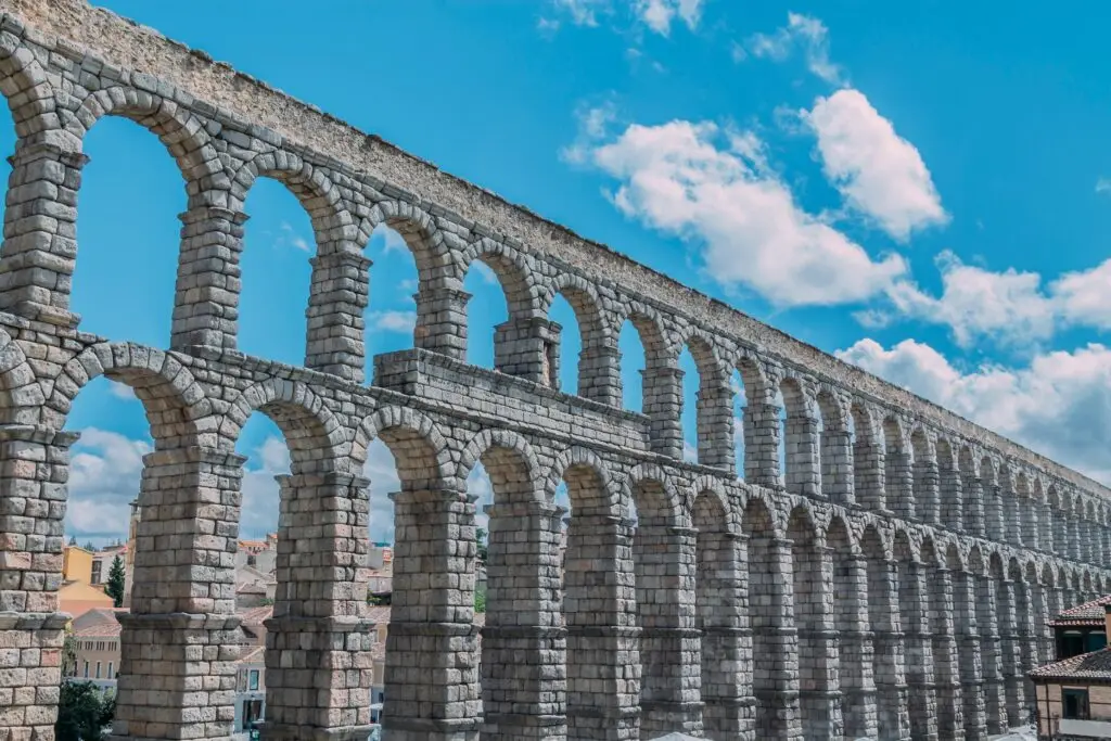 Ancient Roman aqueduct in Segovia Spain with stone arches under a bright blue sky in the historic monumental quarter of Europe
