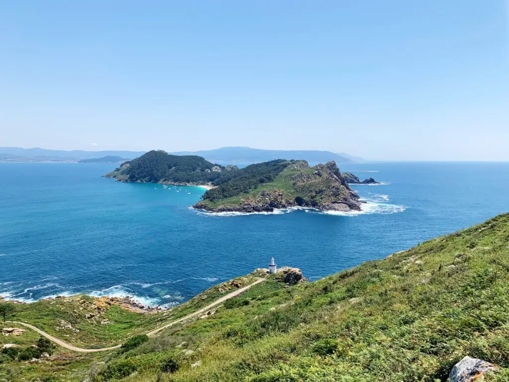 Scenic view of the Cies Islands in Galicia, Spain, featuring rugged coastline, green hills, blue Atlantic Ocean, and a lighthouse, popular destination for nature and beach tourism