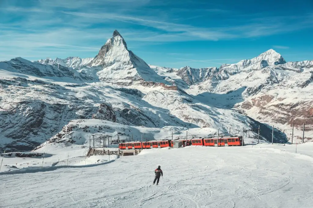 Scenic winter view of the Matterhorn mountain in Switzerland with a skier and red train in the snowy Swiss Alps, popular destination for European private tours and winter holidays