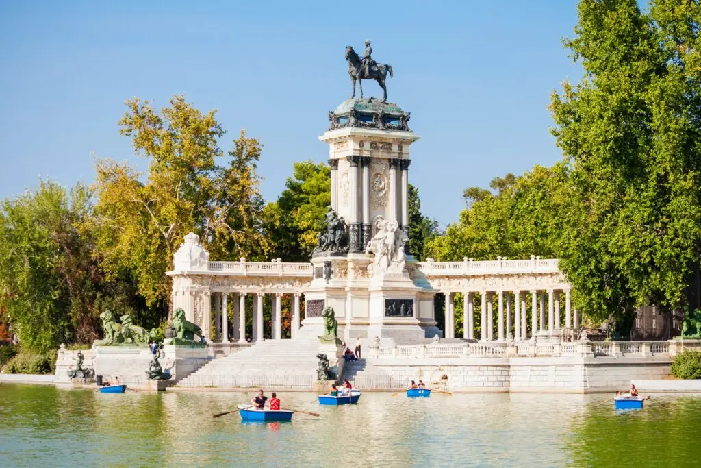 Monument to Alfonso XII in Buen Retiro Park Madrid Spain with people rowing boats on the lake on a sunny day
