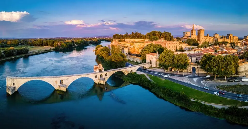 Aerial view of the historic Pont Saint-Bénézet bridge and Palais des Papes in Avignon, France, at sunset over the Rhône River, a popular destination for European private tours.