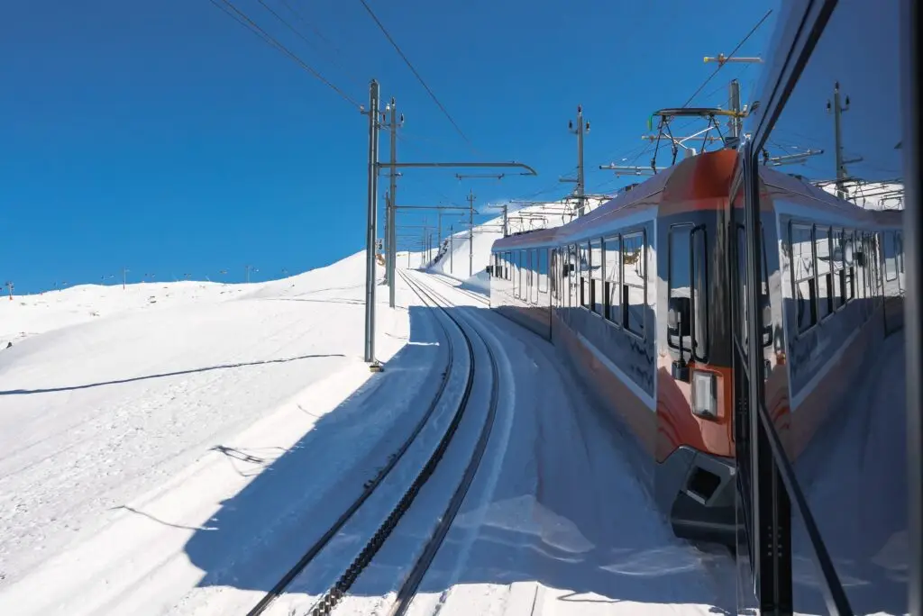 Scenic Gornergrat railway train traveling through snowy Swiss Alps under clear blue sky in Zermatt, Switzerland