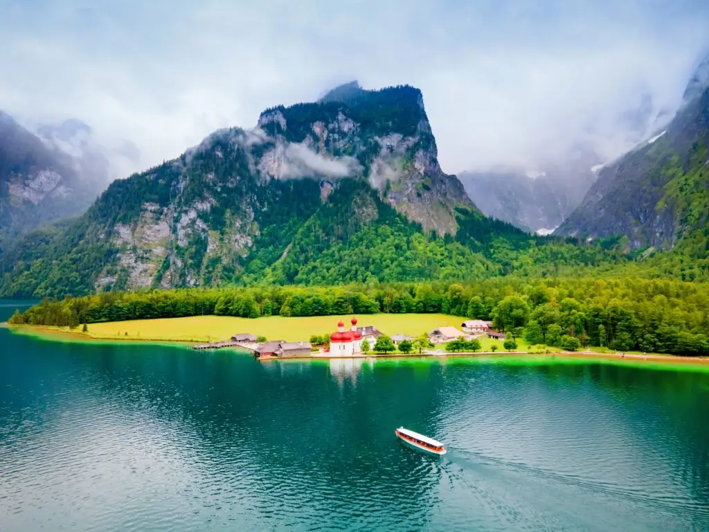 St. Bartholomew Church on Lake Königssee in Bavaria Germany surrounded by alpine mountains and lush forests with a tour boat on the water